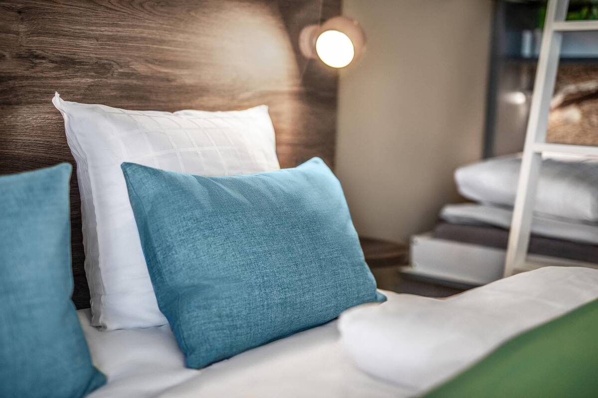 A bed with white and blue pillows, a wooden headboard, and a white nightstand with a lamp.