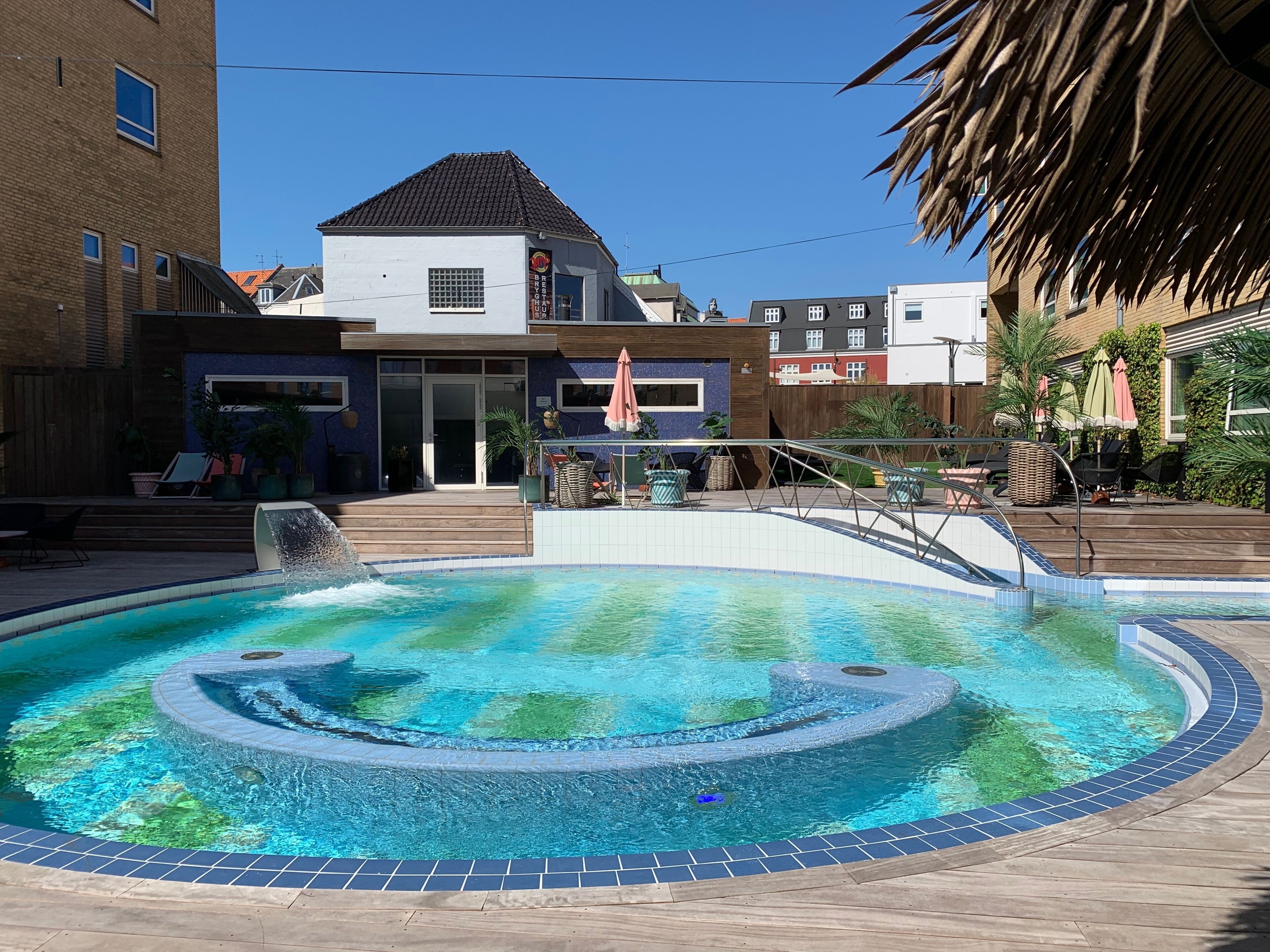 Une piscine avec un jacuzzi, entourée d’une terrasse en bois et agrémentée de plantes en pot.