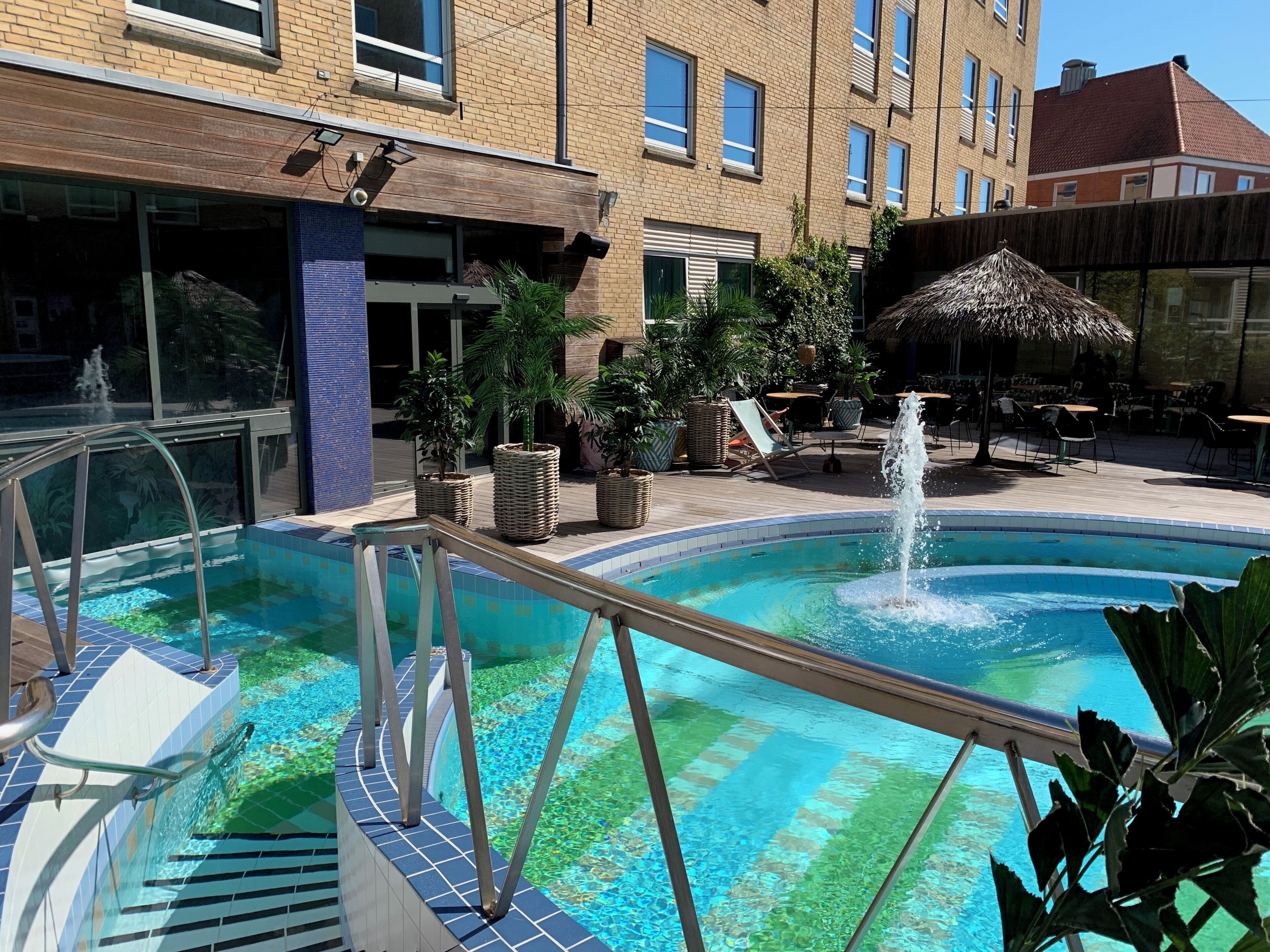 Una piscina con fuente de agua, rodeada de sillones de descanso y plantas en macetas.