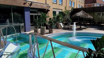 Una piscina con fuente de agua, rodeada de sillones de descanso y plantas en macetas.