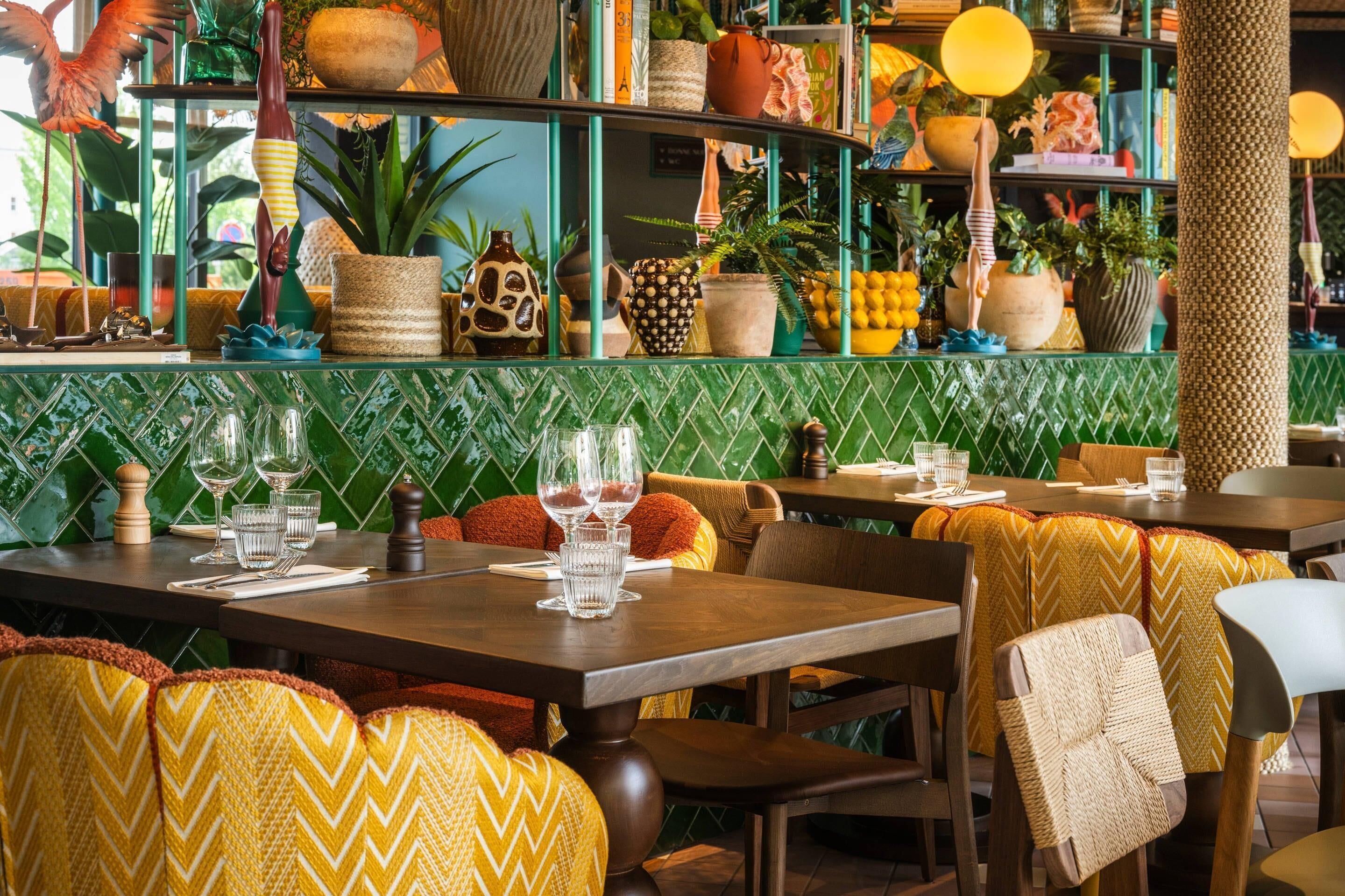 A restaurant interior with green tiled walls, wooden tables, and chairs with patterned cushions.