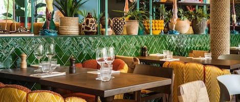 A restaurant interior with green tiled walls, wooden tables, and chairs with patterned cushions.
