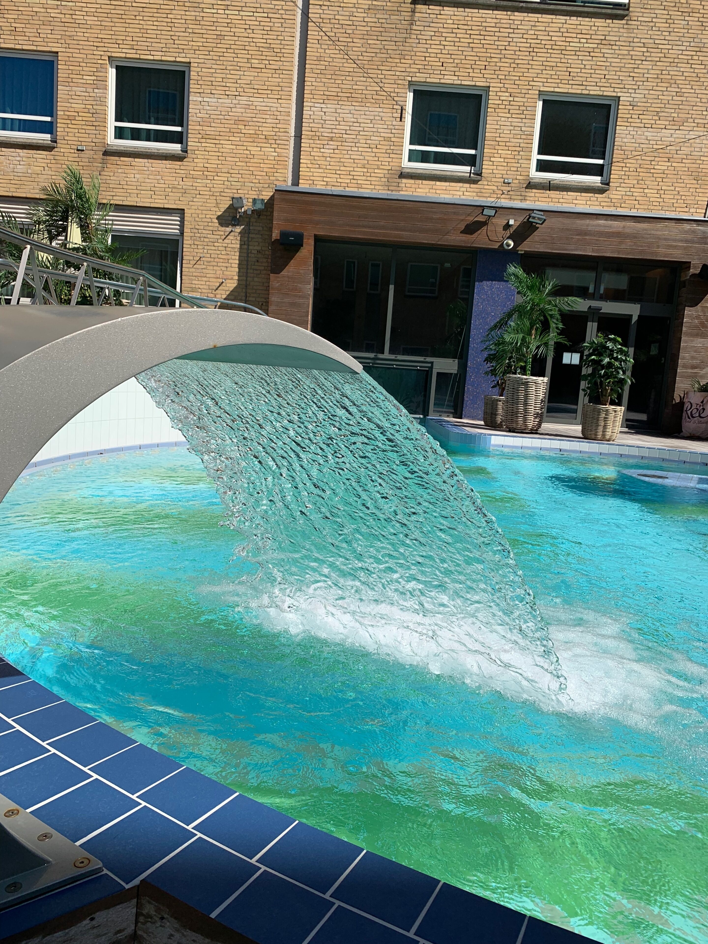 A swimming pool with a clear water surface, surrounded by a building with a brick facade and multiple windows.