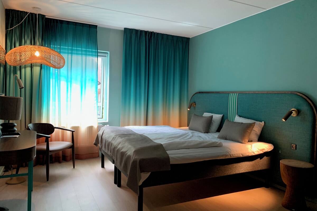 A bedroom with a bed, a desk, a chair, and a lamp.