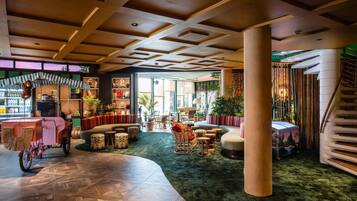 A spacious lobby with a green carpet, wooden flooring, and a variety of seating options including sofas and chairs.