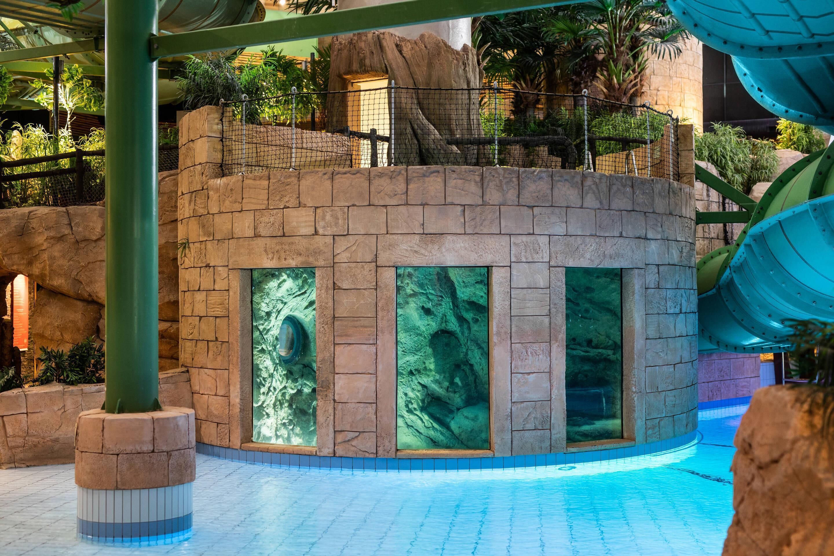 Un edificio circular con una fuente de agua, rodeado por una piscina y vegetación.