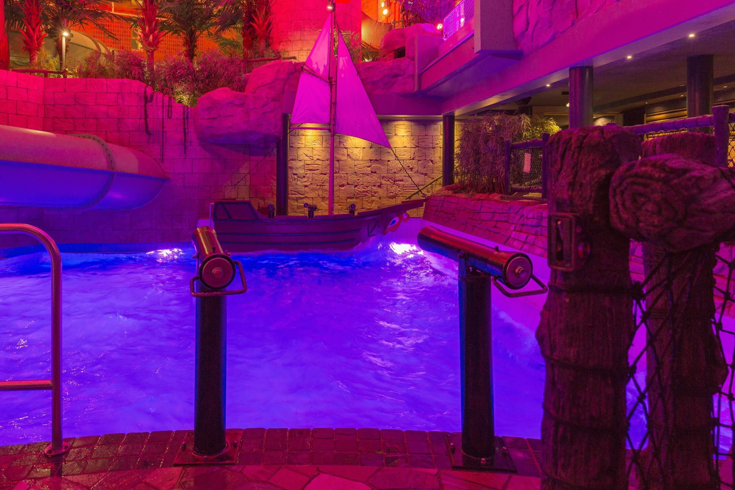 An indoor pool area with a ship-themed design, including a ship model and a stone wall backdrop.