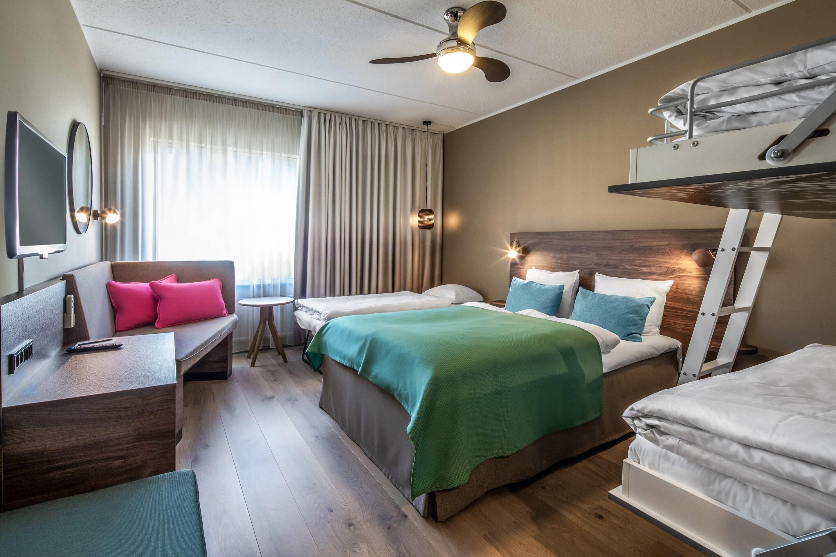 A hotel room with a bed, a desk, a chair, a bunk bed, and a ceiling fan.