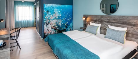 Habitación de hotel moderna con una cama grande, cabecera de madera, un cuadro abstracto de gran tamaño, un espejo redondo y una zona de comedor con mesa y sillas.