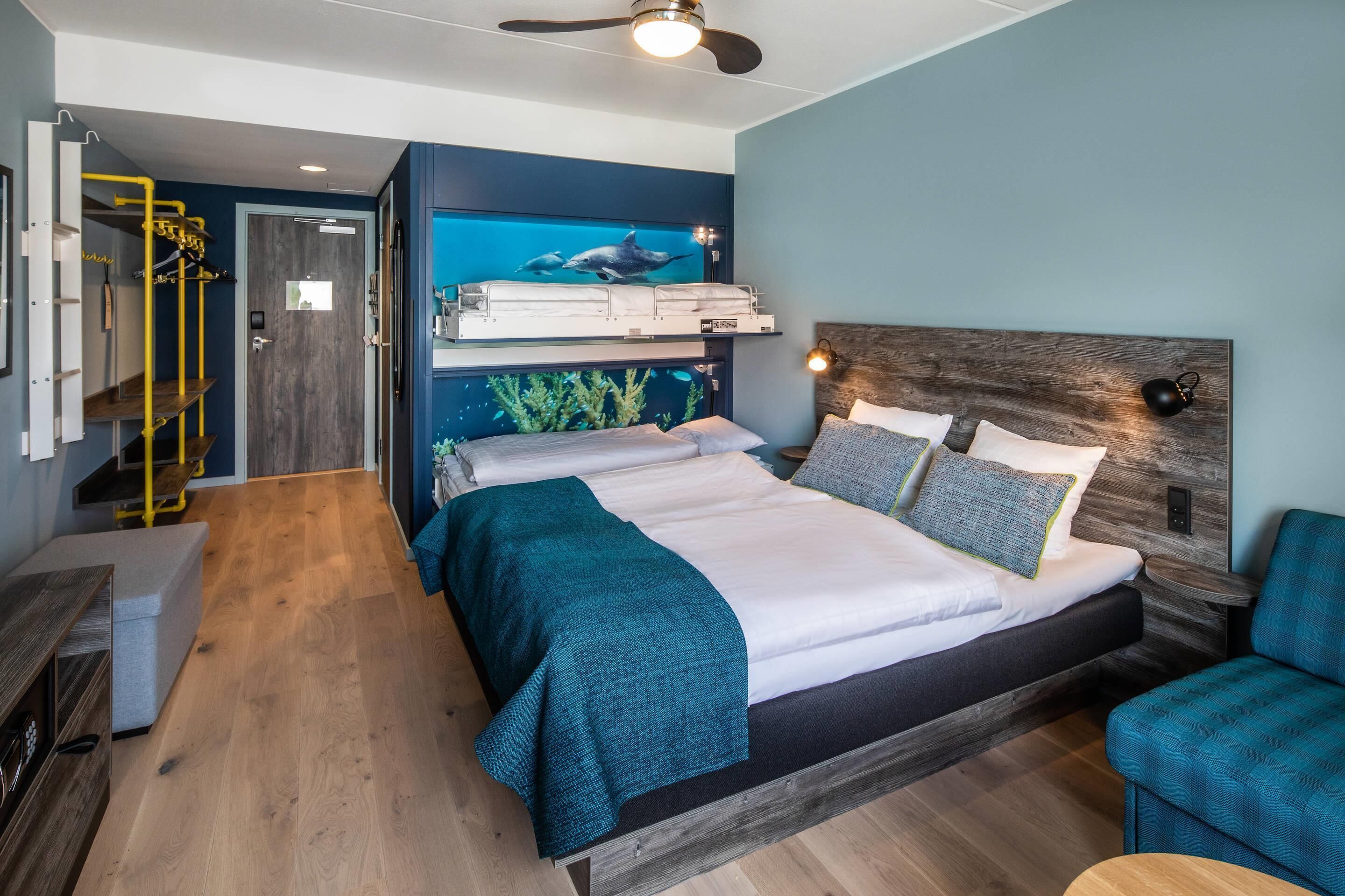 Een slaapkamer met een stapelbed, een plafondventilator, een wandaquarium en een zithoek met een blauwe stoel.