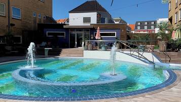 Una piscina con dos fuentes, rodeada por un muelle de madera y un edificio con un cartel que dice 'Quality Hotel'.