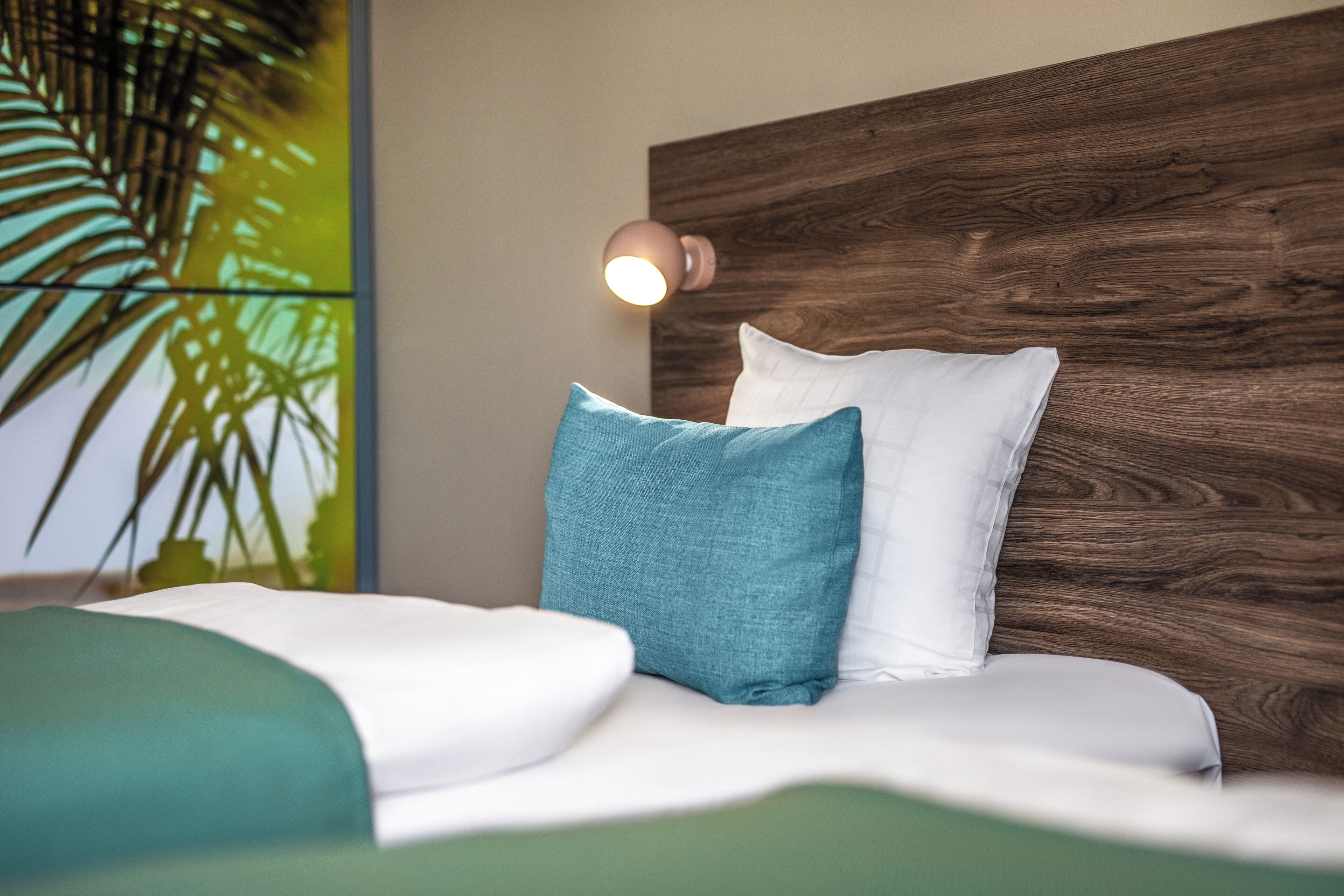 A bed with white and teal bedding, a wooden headboard, and a wall-mounted lamp.