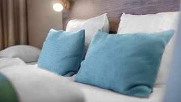 A bed with white bedding and two blue pillows.