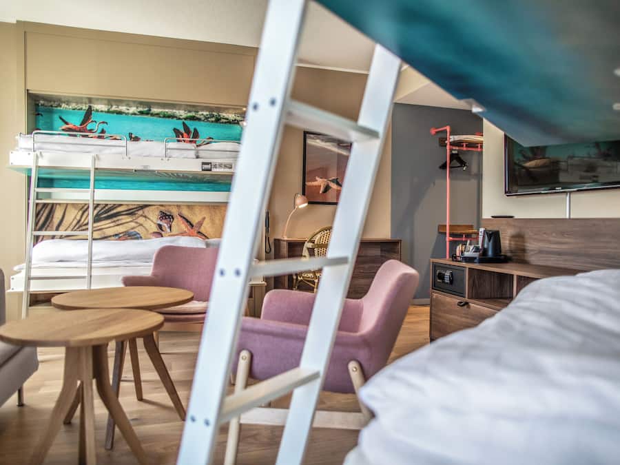 A hotel room with bunk beds, a desk, a chair, a small table, and a TV.