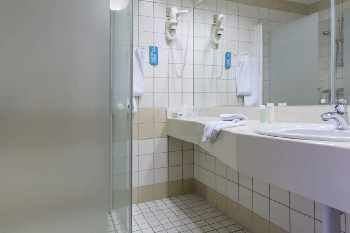 A bathroom with a glass shower enclosure, a sink, and a mirror.