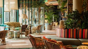 A spacious lounge area with wicker furniture, a striped sofa, and various potted plants. - Quality Hotel The Reef (Frederikshavn)