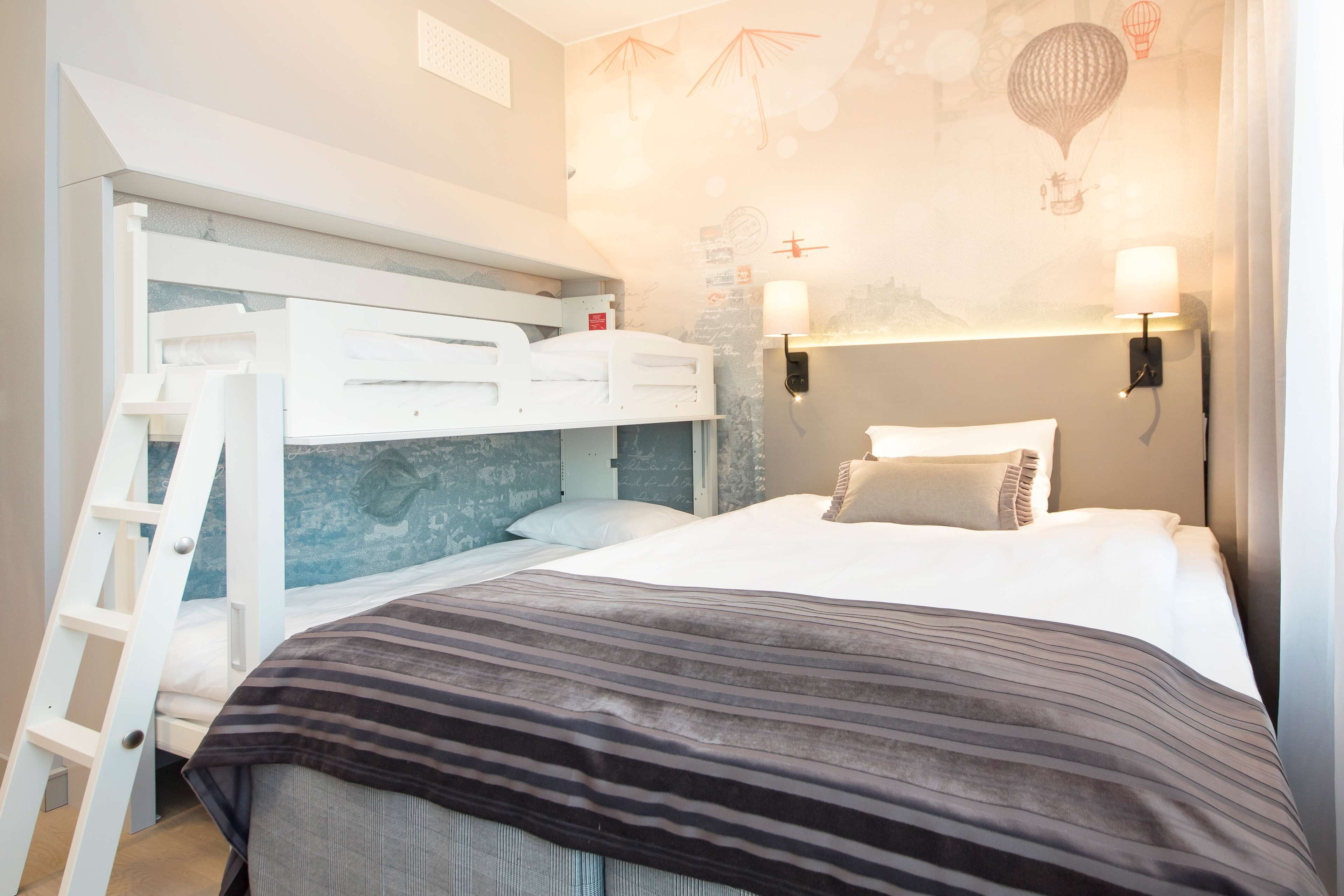 A bunk bed room with a ladder, two bedside lamps, and a striped blanket.