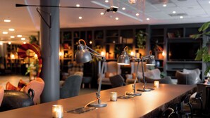 Zona de bar moderna con varias lámparas colgantes, una barra larga y taburetes.