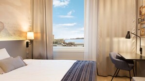 Una habitación de hotel con una cama, un escritorio, una silla, una lámpara y vistas al agua y edificios.
