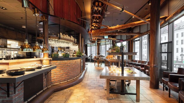 Un restaurante moderno con una zona de bar de ladrillo, suelo de baldosas hexagonales y amplios ventanales con vistas a la ciudad.
