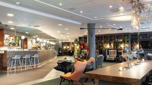 Un interior moderno con zona de bar, asientos y una gran planta decorativa.