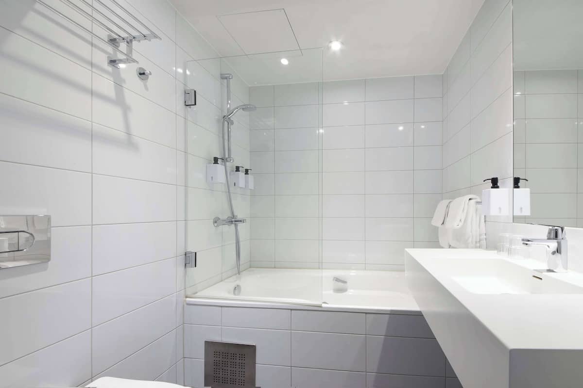 A modern bathroom with a glass-enclosed shower, a white bathtub, and a vanity with a sink and mirror.