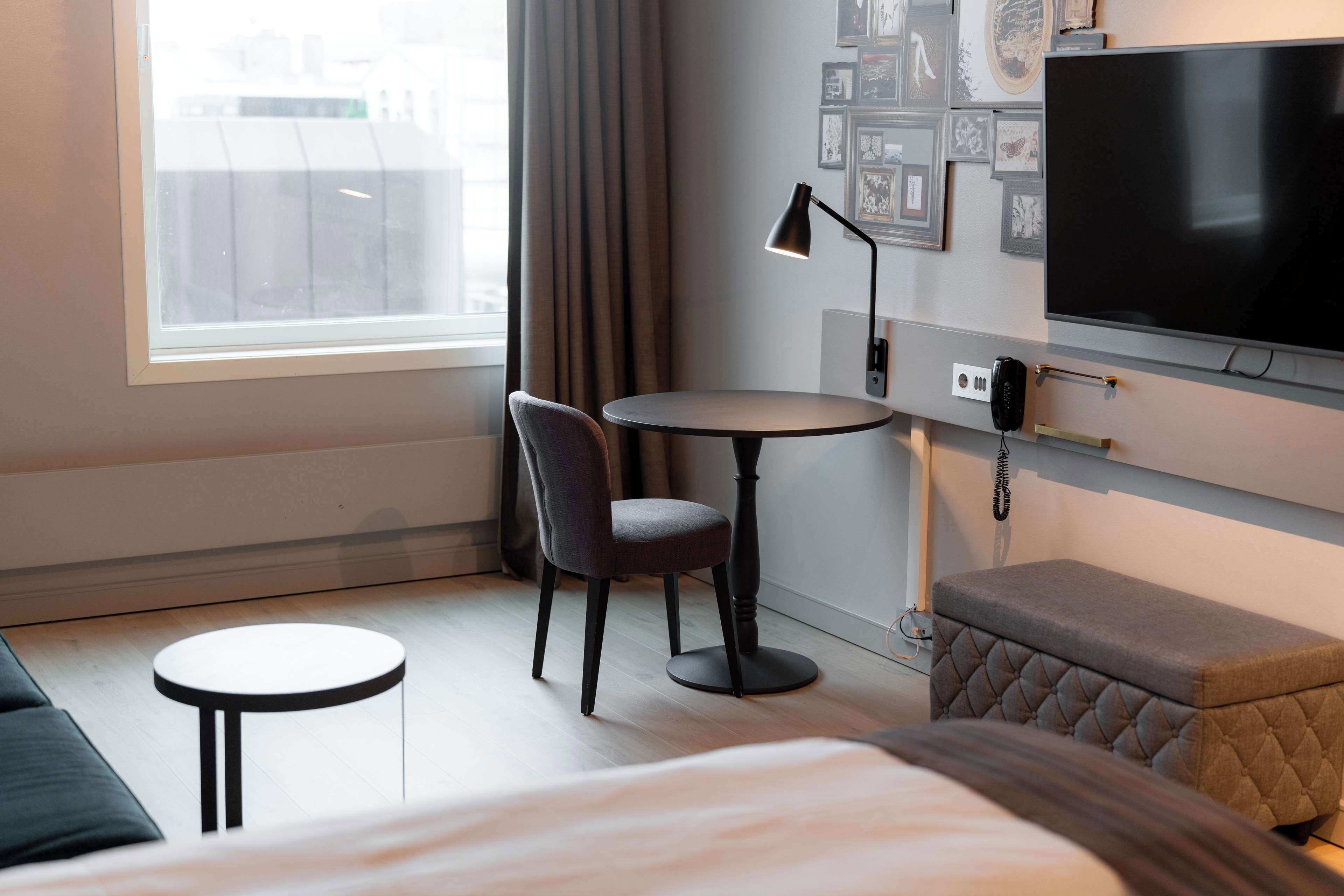 Una habitación de hotel con una cama, una mesa redonda con una silla, un televisor y un pequeño otoman.