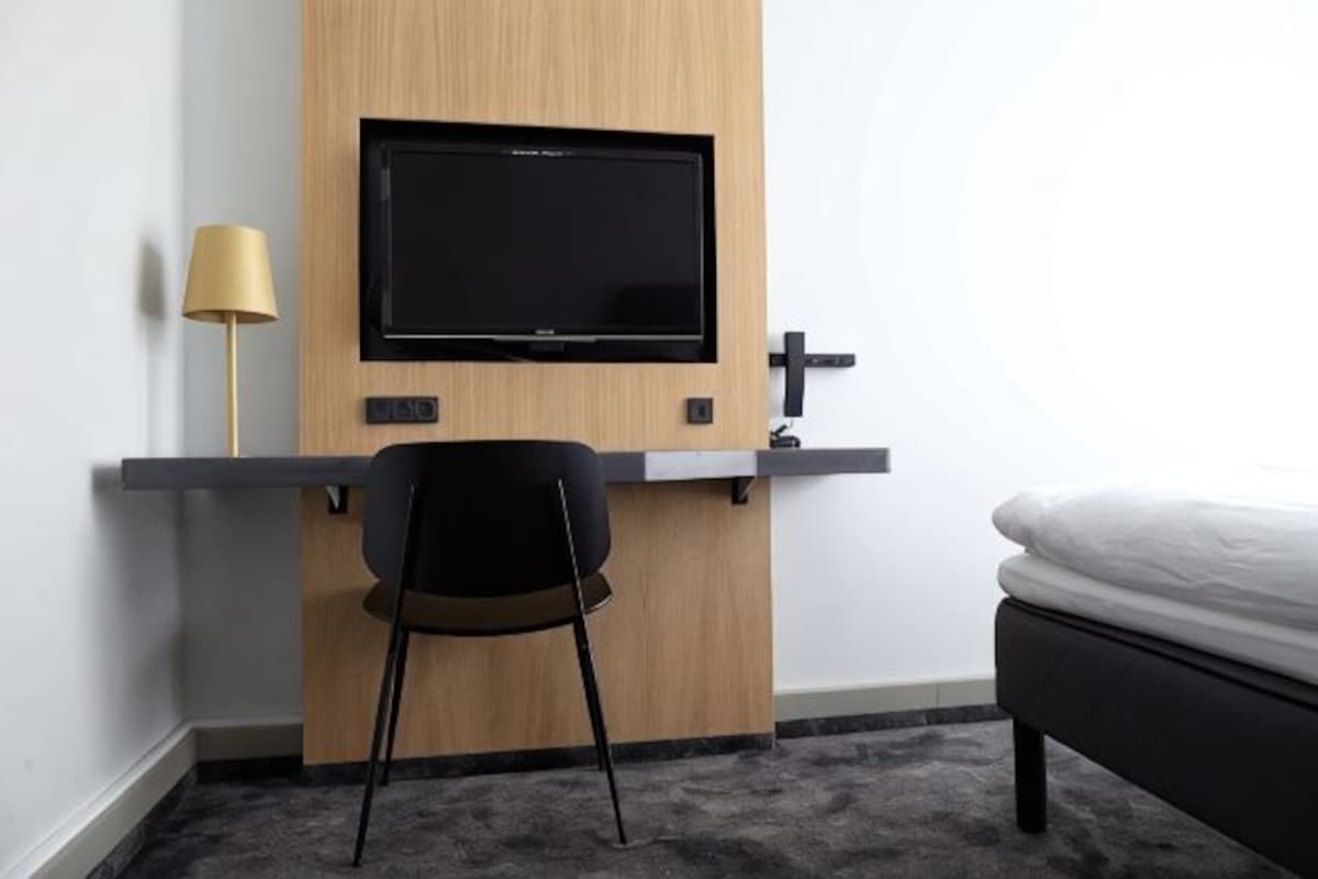 A room with a bed, a desk with a TV, a lamp, and a chair.