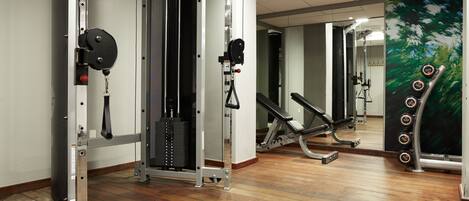 A gym with weightlifting equipment, a mirror, and a wooden floor.