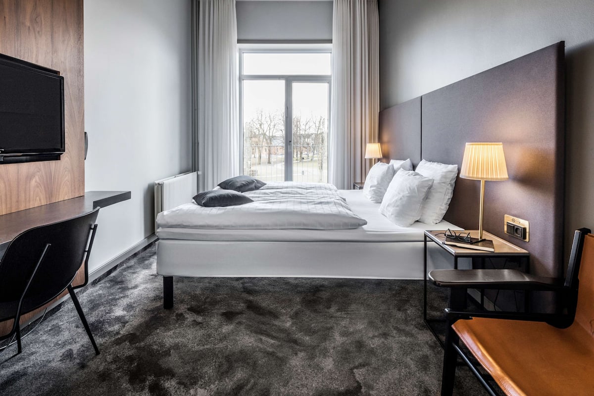 Hotellihuone, jossa on sänky, yöpöytä, lamppu ja seinälle asennettu televisio.