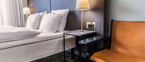 A hotel room with a bed, two bedside lamps, a small table, and a chair.