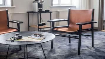 A room with two leather chairs, a round table with a camera, glasses, and a book, and a coffee machine on a small table.
