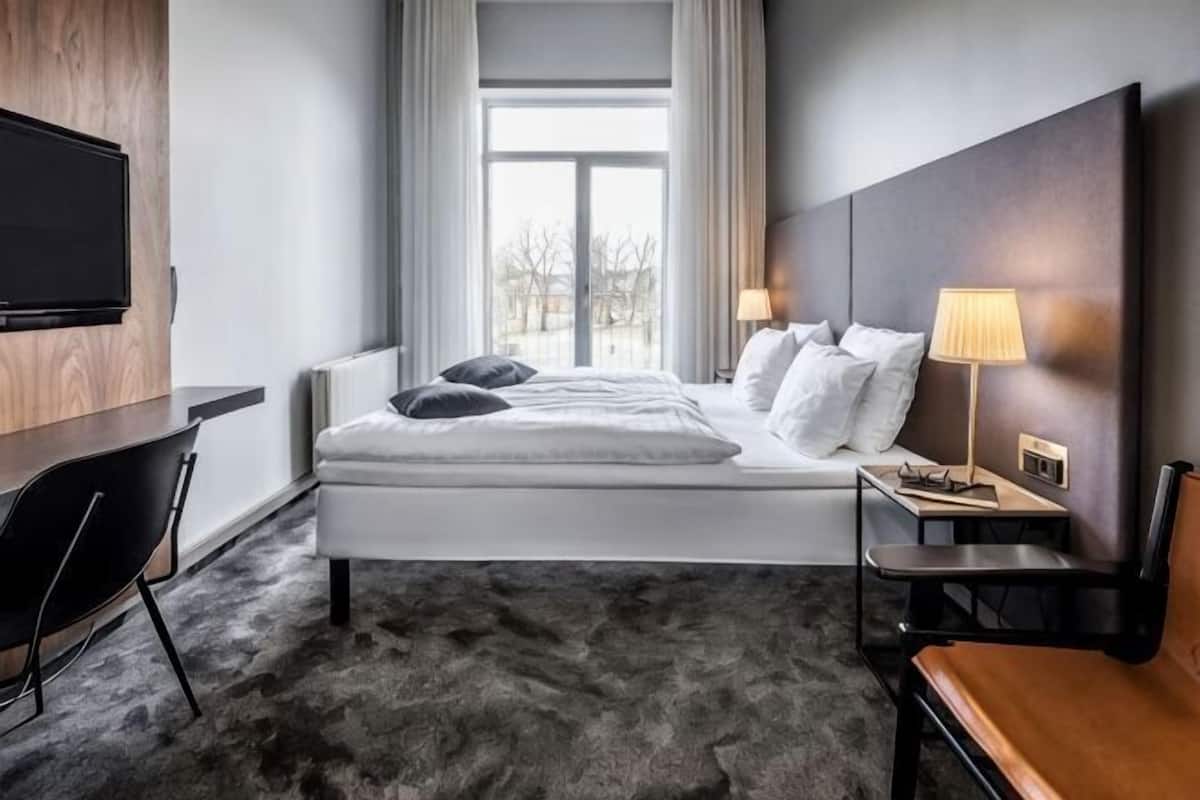 Moderni hotellihuone, jossa on sänky, yöpöydät, työpöytä ja televisio.