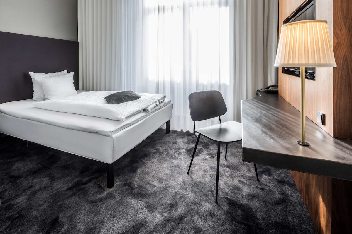 Hotellihuone, jossa on sänky, tuoli, työpöytä ja lamppu.