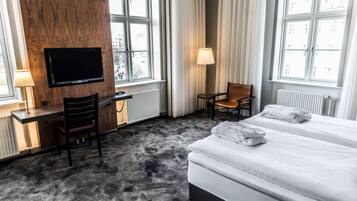 Una habitación de hotel con cama, escritorio, silla, televisor y ventanas amplias.