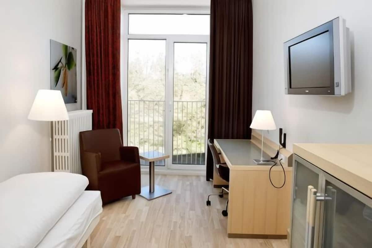 Hotellihuone, jossa on sänky, työpöytä, tuoli, televisio ja ikkuna, jossa on verhot.