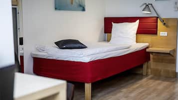 A neatly made bed with a red headboard, a bedside table with a lamp, and a wooden nightstand.