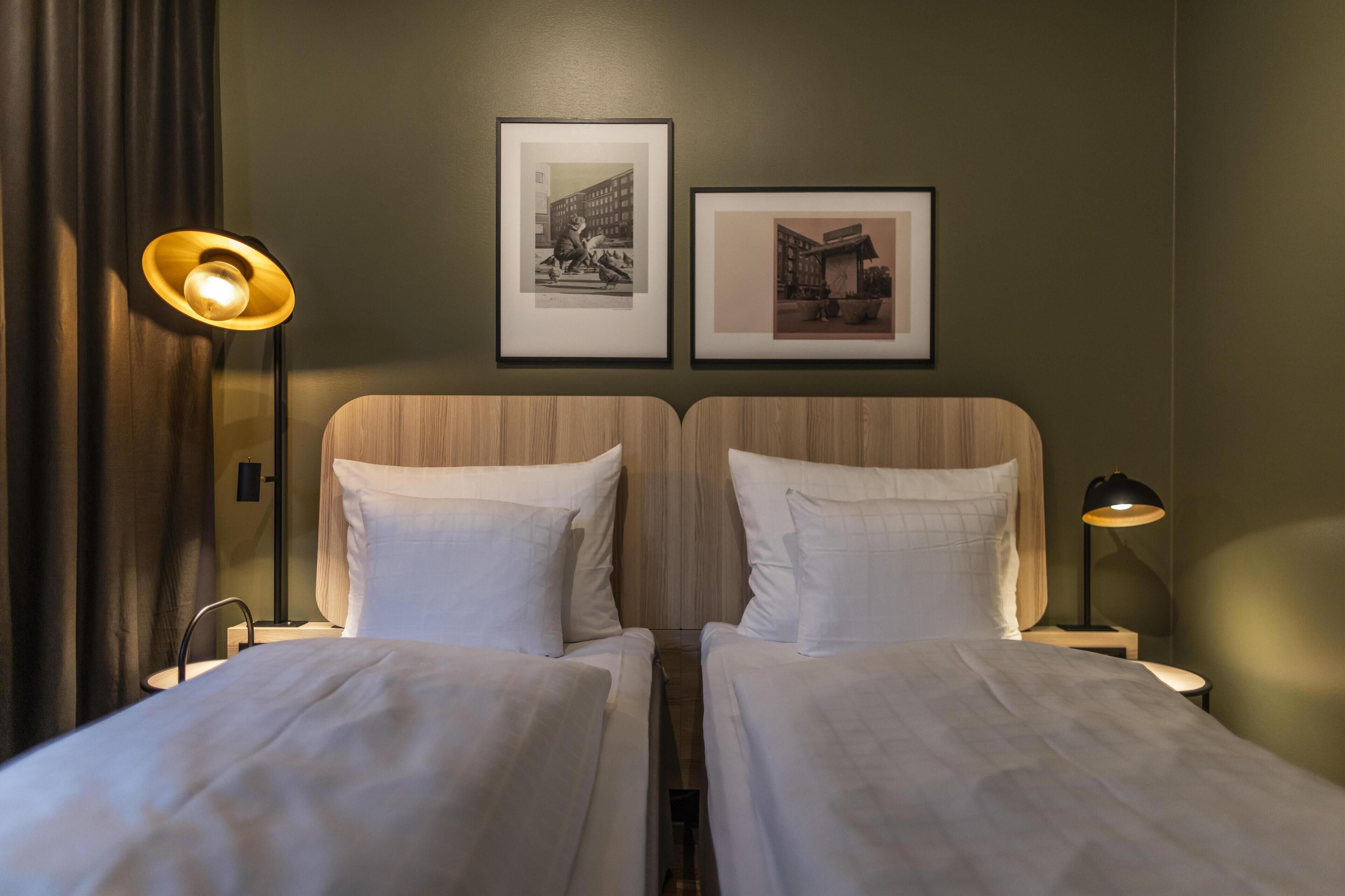 Une chambre d’hôtel avec deux lits, une table de chevet avec une lampe et deux tableaux encadrés au mur.