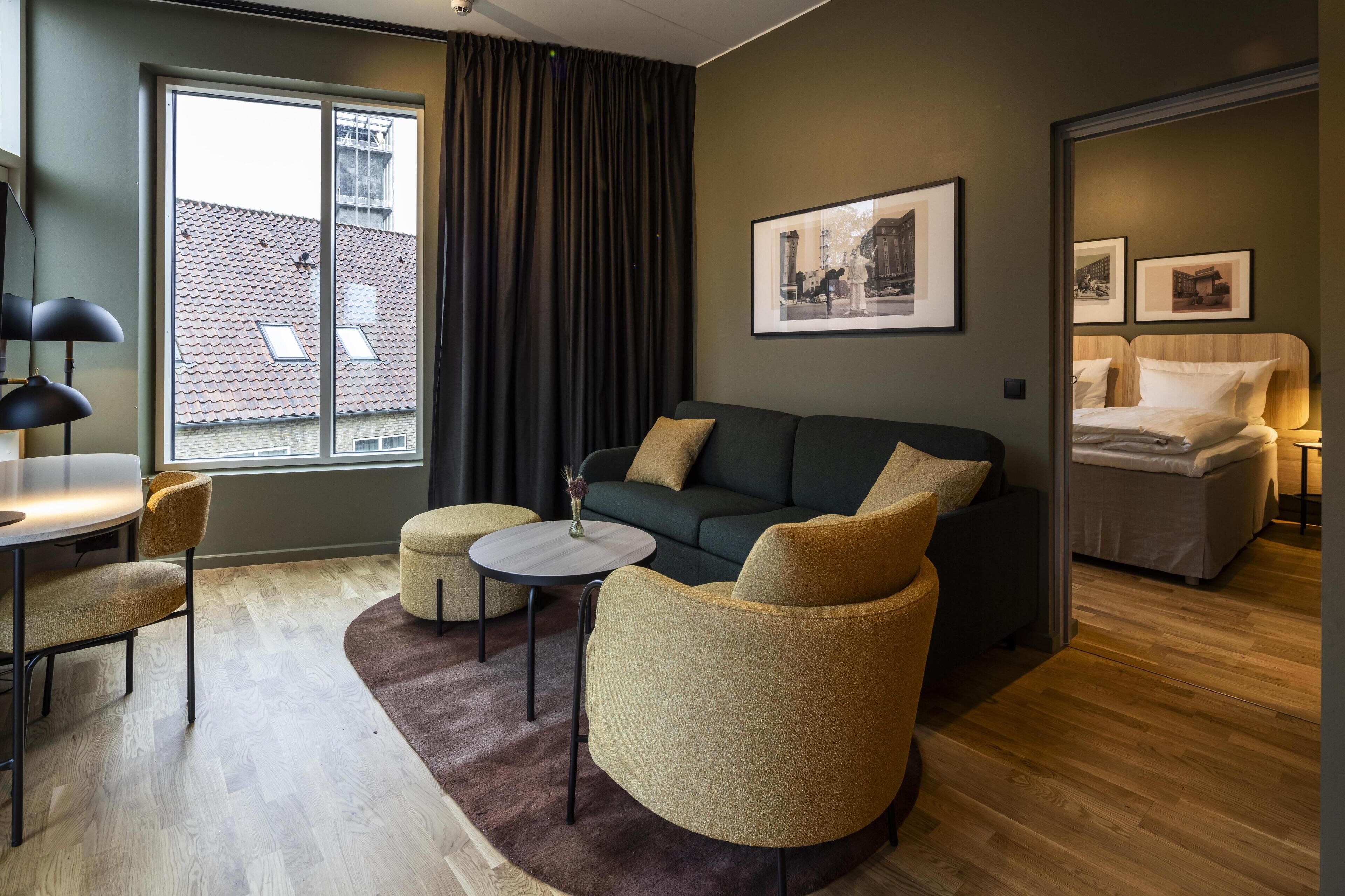 A modern living room with a sofa, armchairs, a small round table, and a dining area with a chair.