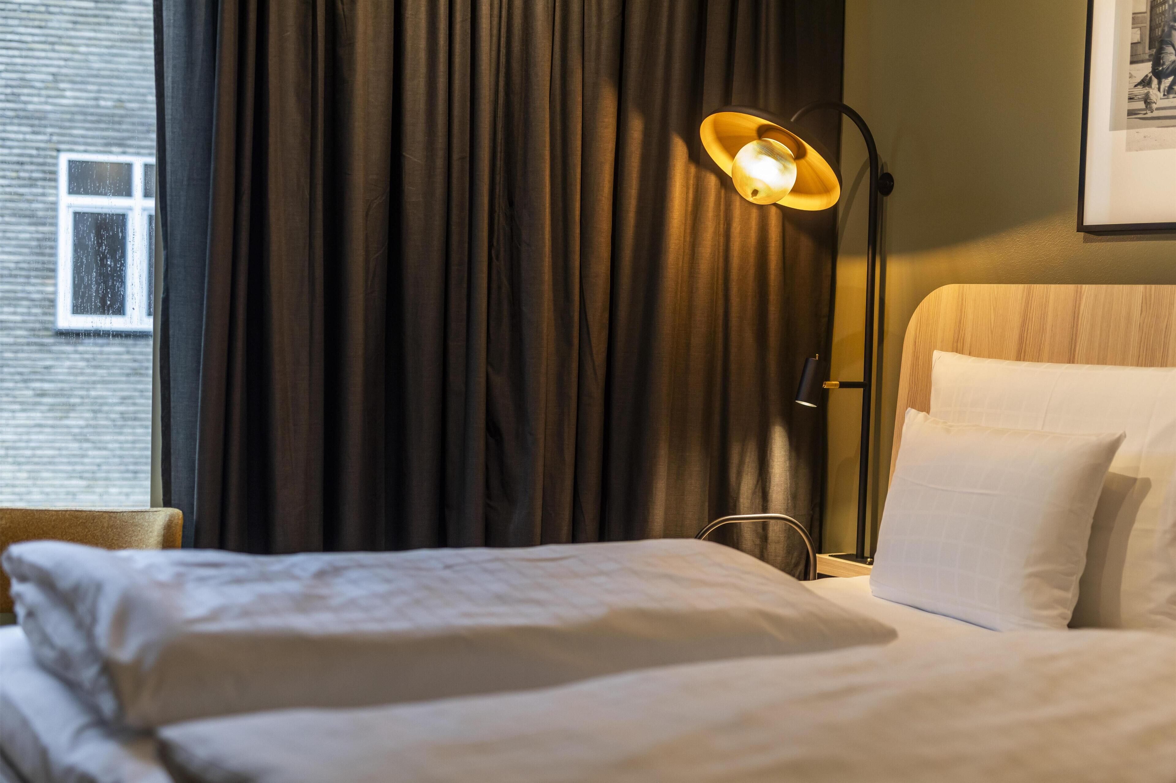 A hotel room with a bed, a lamp, and a window with curtains.