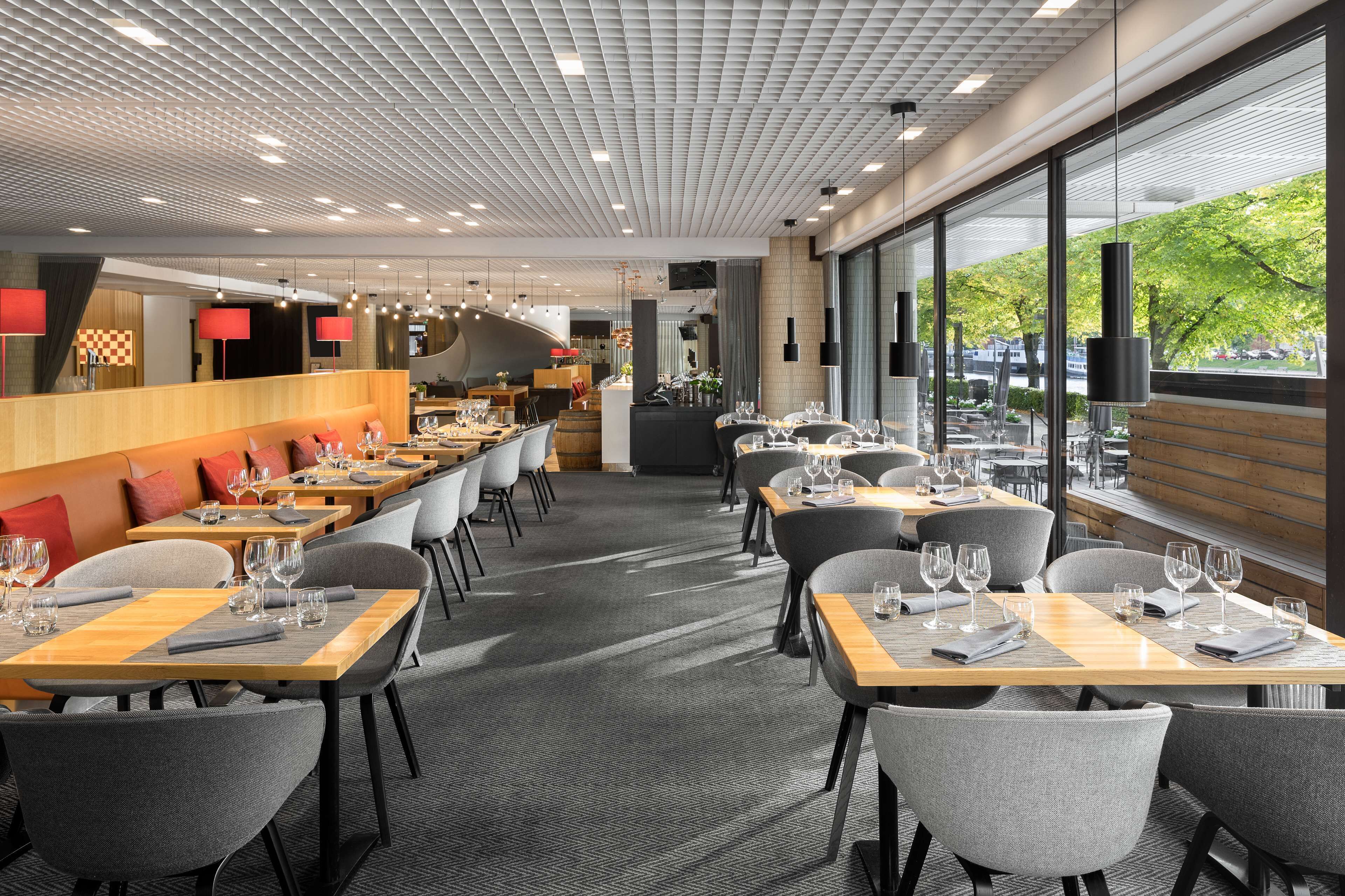 Un restaurante moderno con una barra larga, varias mesas y vistas al exterior.