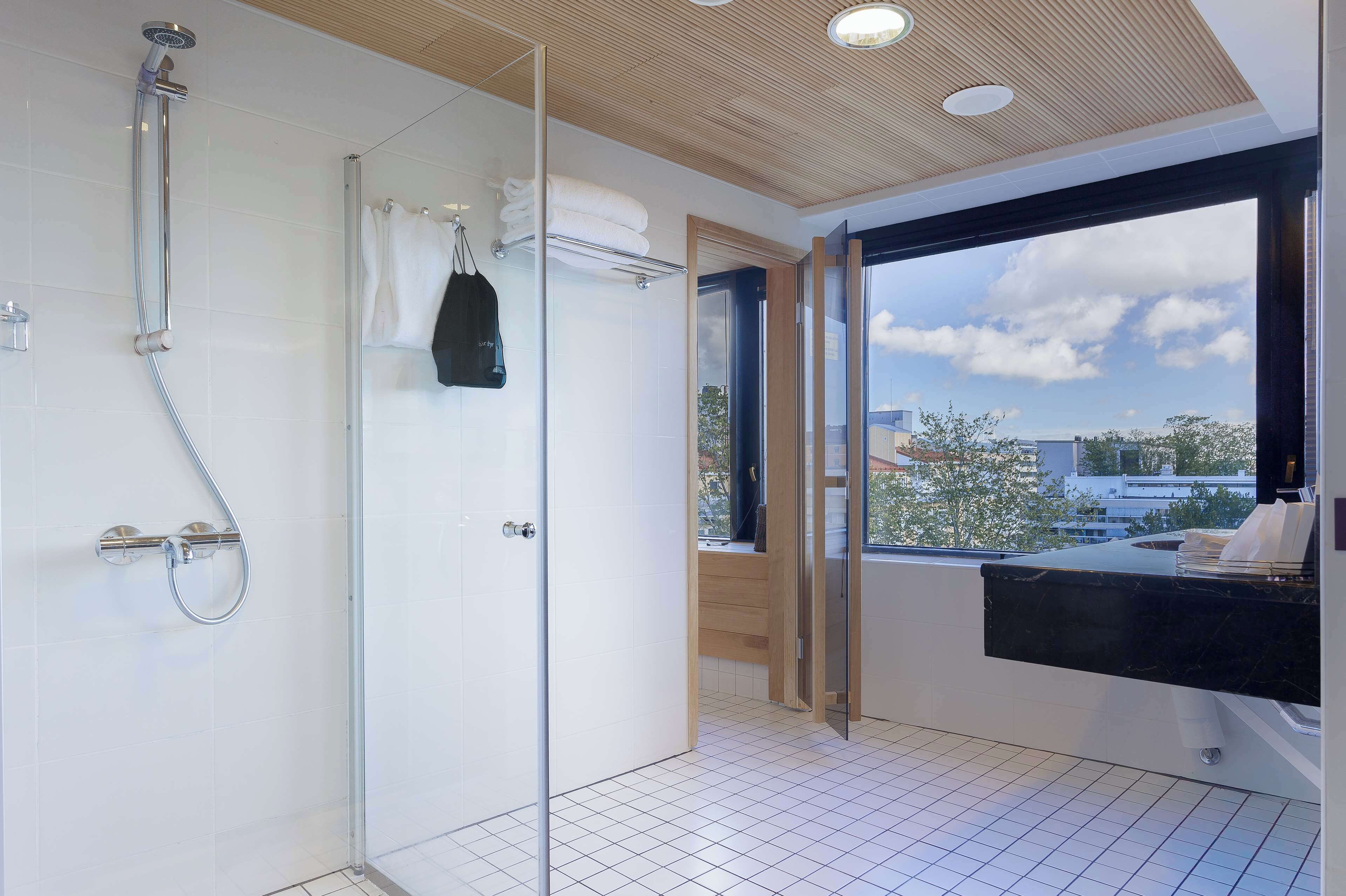 Un baño moderno con cabina de ducha de vidrio, encimera de mármol negro y vistas a la ciudad a través de un amplio ventanal.