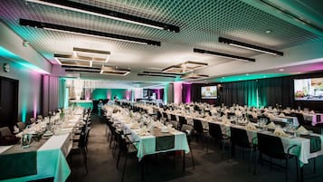 A large banquet hall with long tables set for a formal event, featuring a modern ceiling design and ambient lighting.