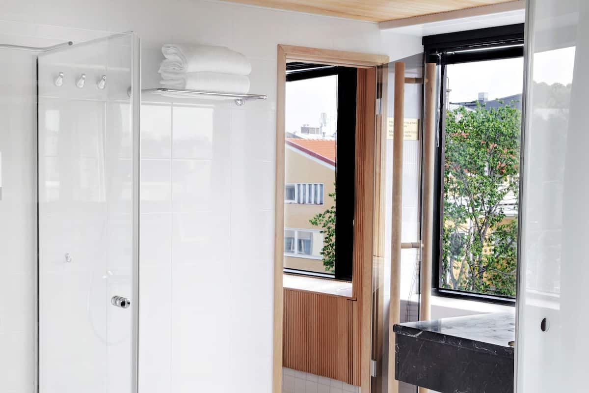 Ein modernes Badezimmer mit Duschkabine aus Glas, einem Handtuchhalter und Ausblick ins Freie durch ein großes Fenster.