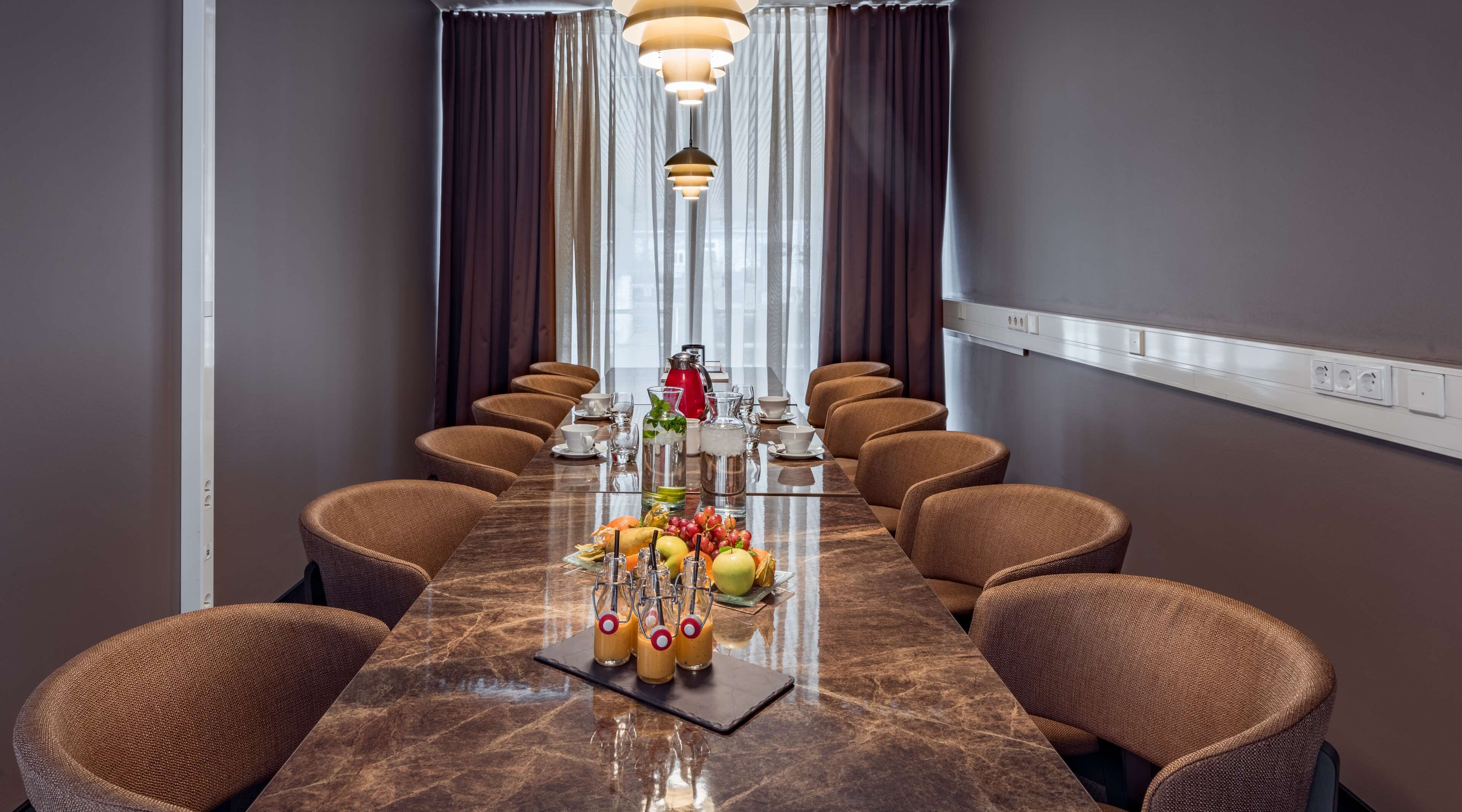 A conference room with a long table, brown upholstered chairs, and a marble floor.