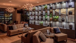 En moderne lobby med sofaer, et sofabord og en væg med dekorative vaser og planter.