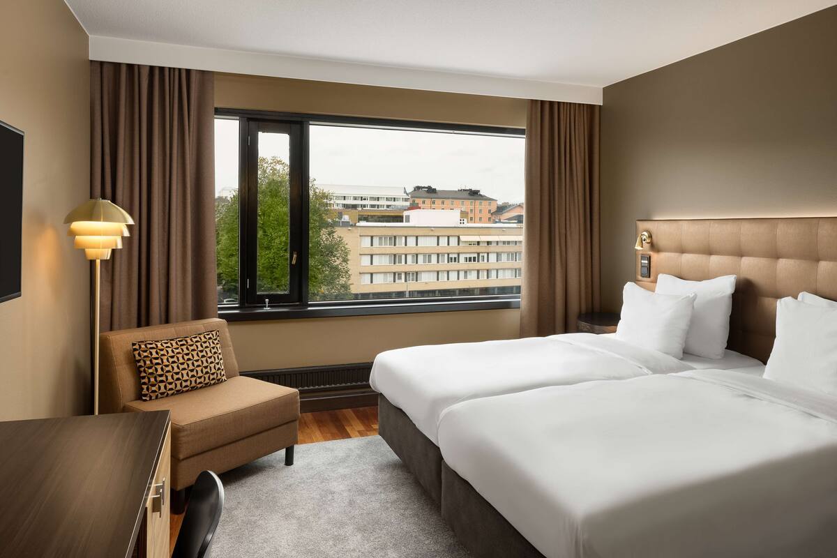 Ein Hotelzimmer mit großem Fenster, einer Couch, einem Schreibtisch und einem Bett mit weißer Bettwäsche.