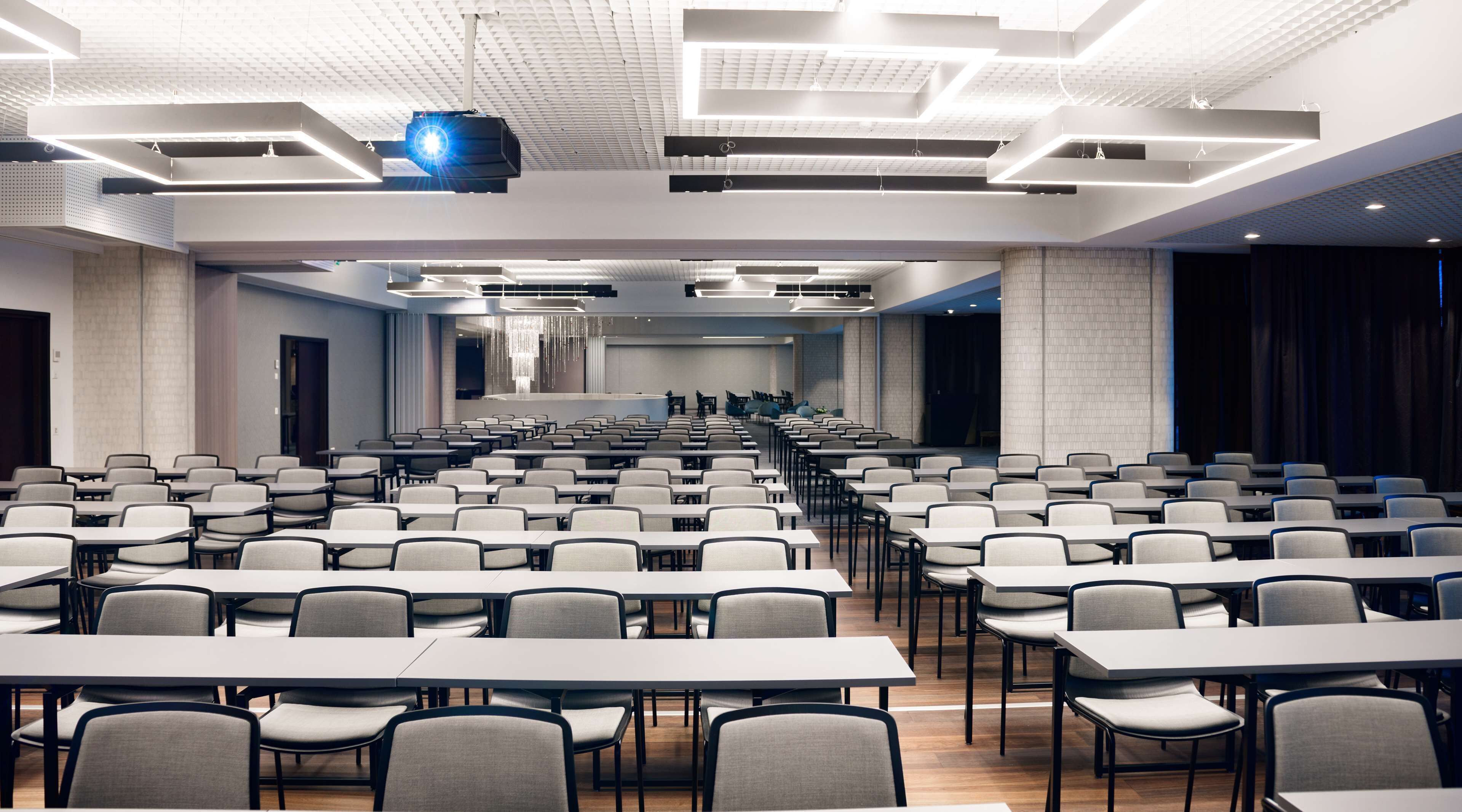 A conference room with rows of tables and chairs, a large screen, and a modern ceiling design.