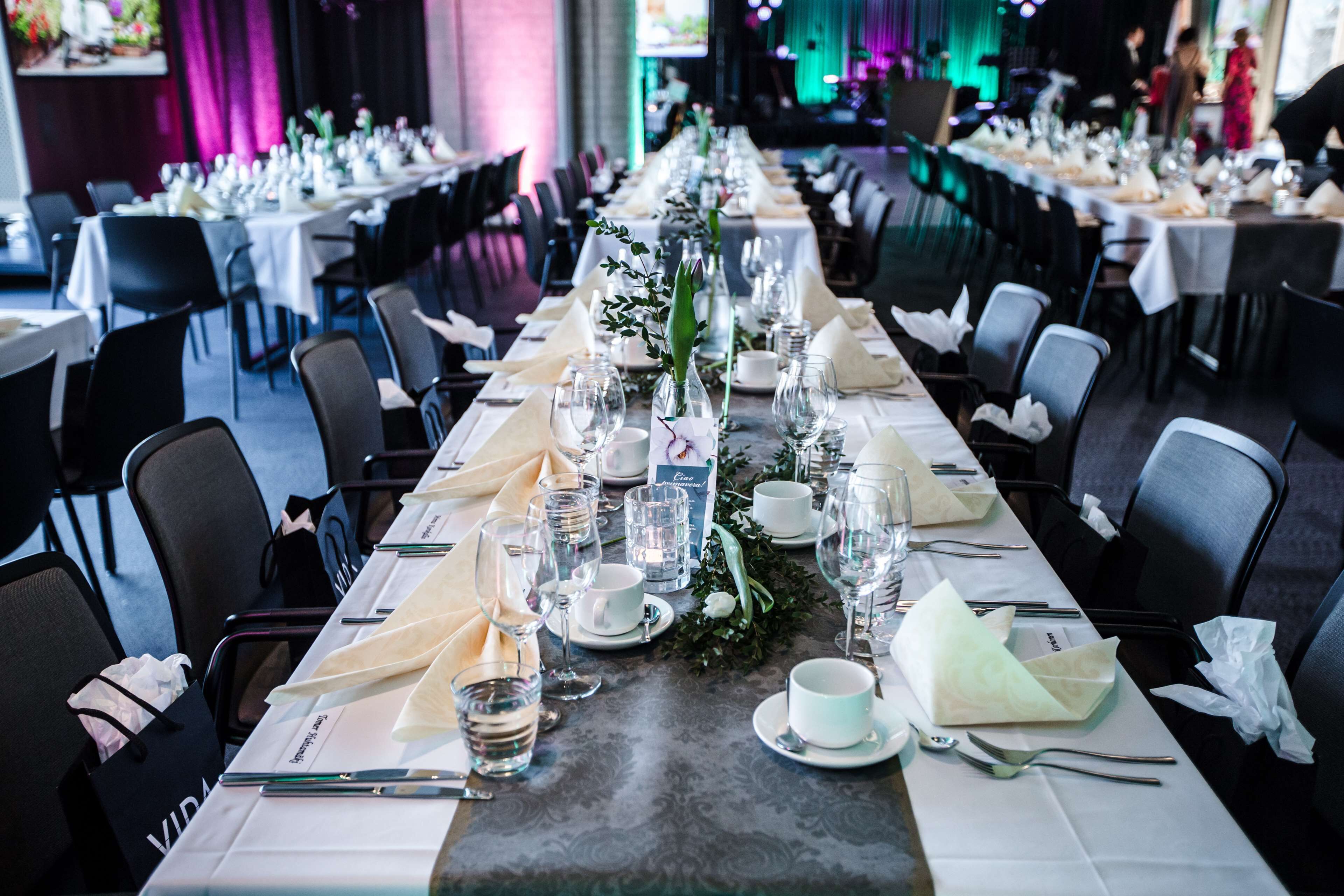 A long dining table set with white tablecloths, glassware, and napkins.