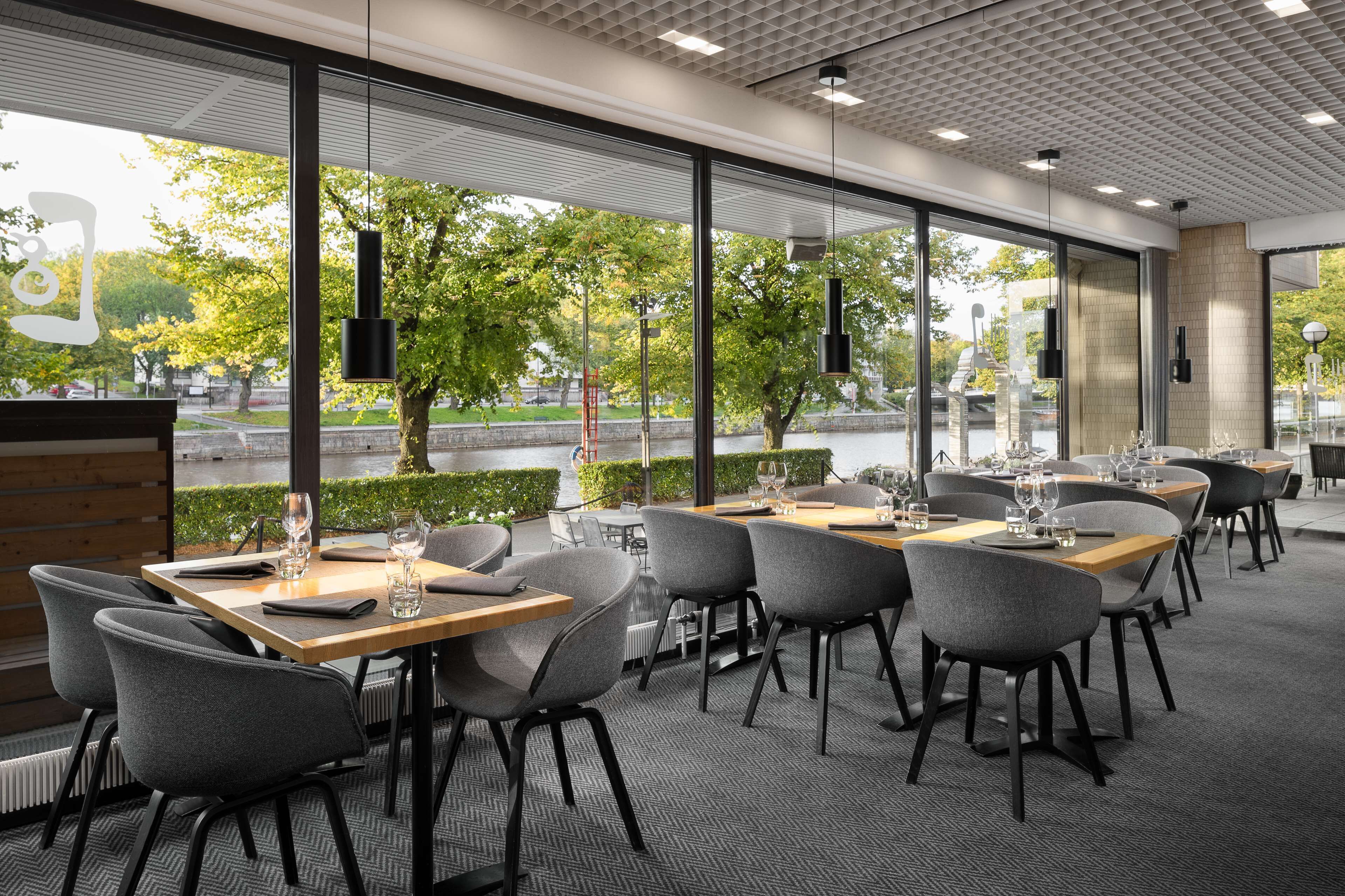 Un restaurant moderne avec de grandes fenêtres, des chaises à revêtement gris et des tables soigneusement dressées.
